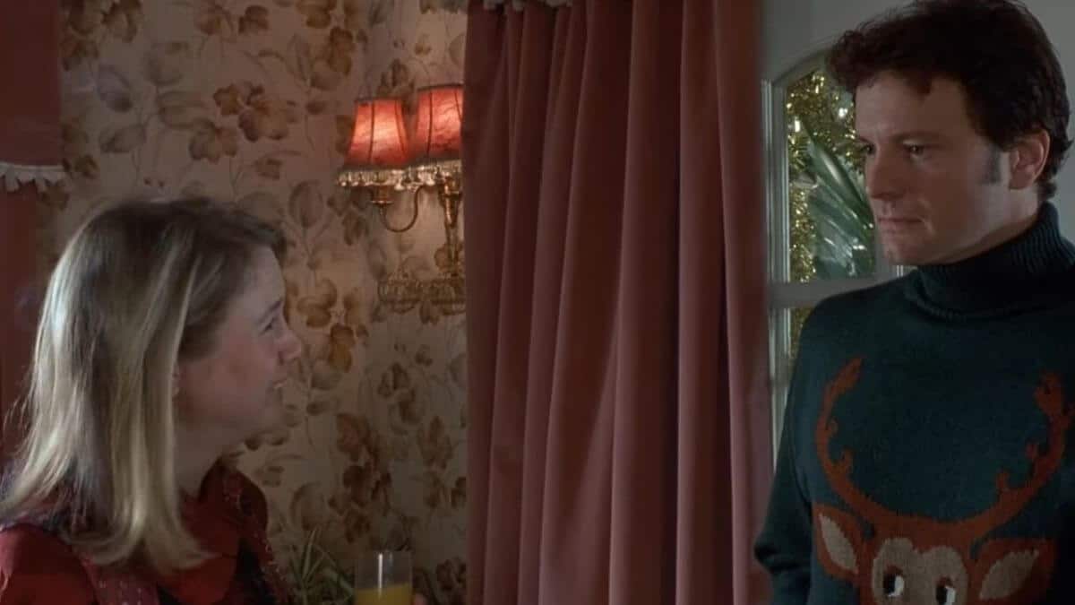 Colin Firth as Mark Darcy wearing the Christmas reindeer sweater. Bridget Jones stands next to him.