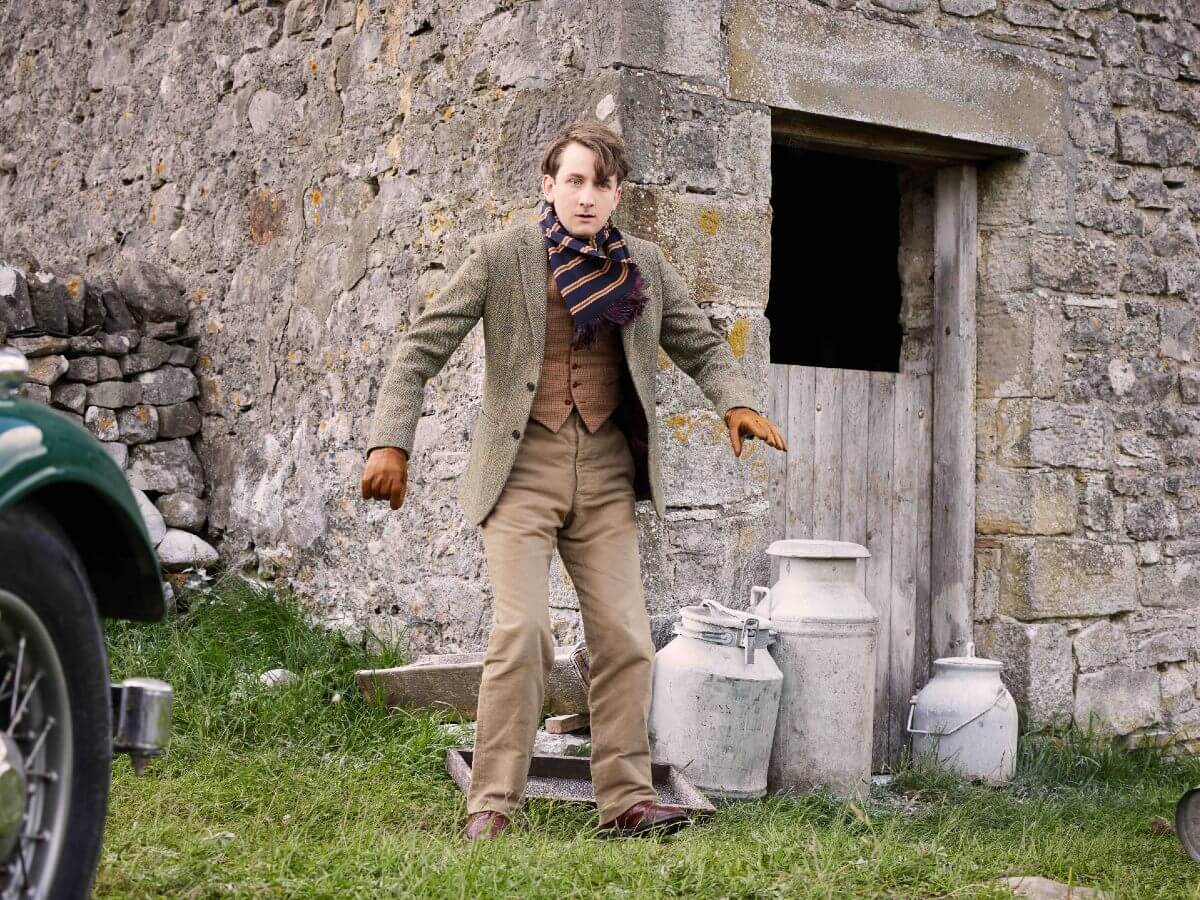 James Anthony-Rose as Richard Carmody in All Creatures Great and Small Season 4. He's outside in front of a farm wearing 1940s period costume.